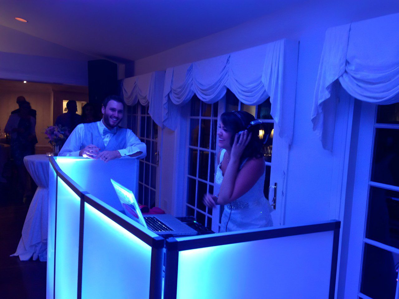 A Man and Woman Dancing at a Party With a DJ Booth in the Background.