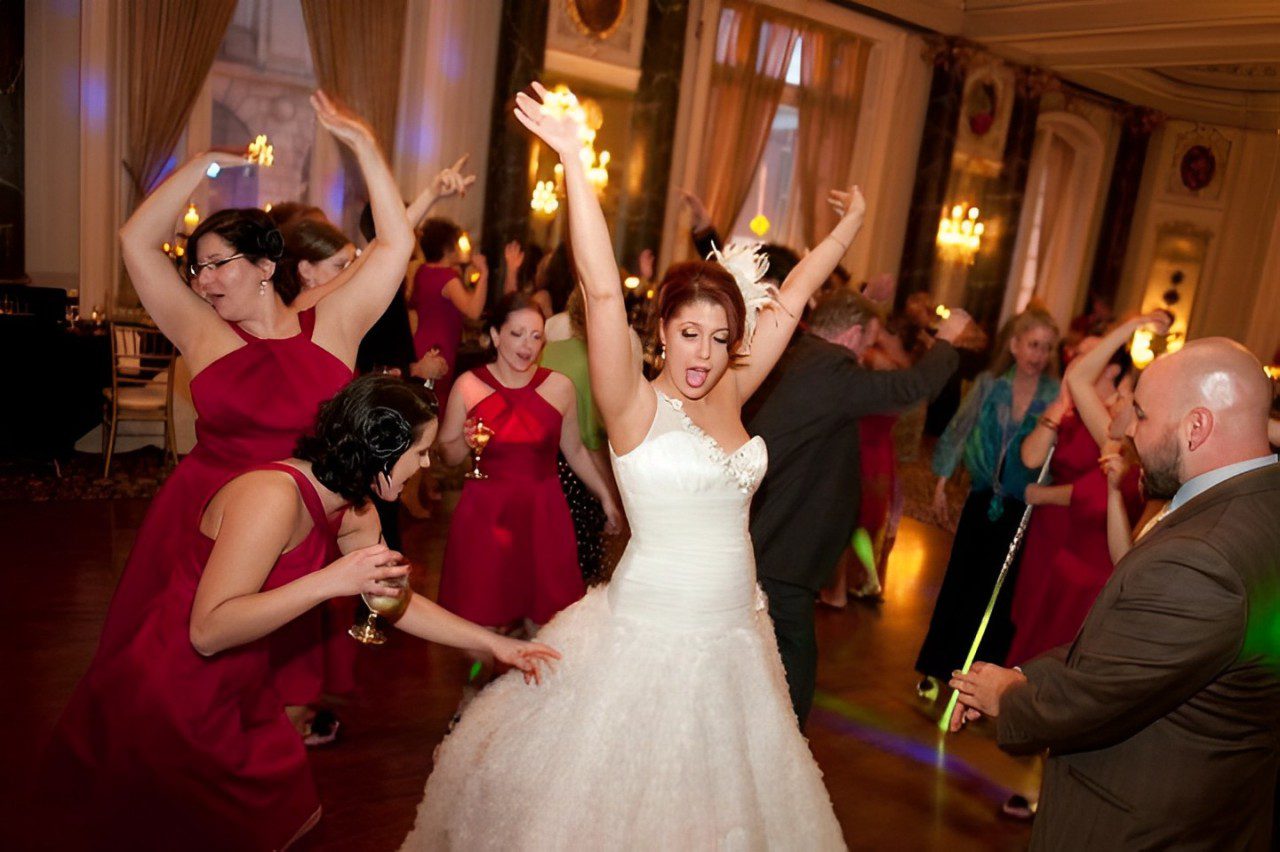 A Bride and Groom Dancing Joyfully in the Center of a Spacious Room, Surrounded by Their Friends and Family.