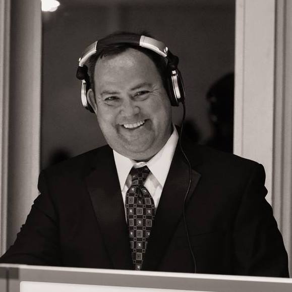 A Man in a Suit and Tie Smiling While Wearing Headphones.