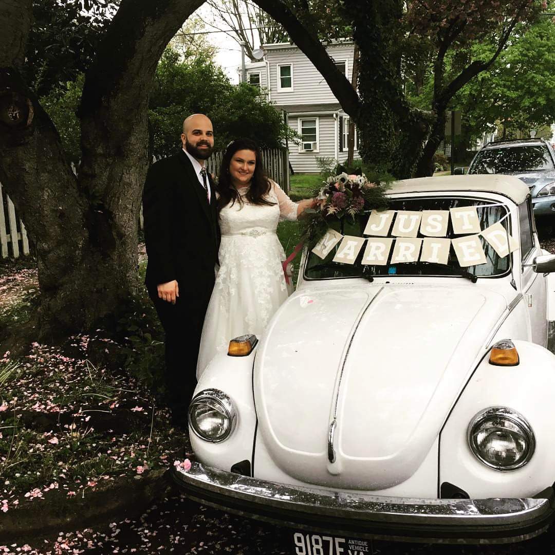 A Bride and Groom Smiling in Front of a White VW Bug on Their Wedding Day.